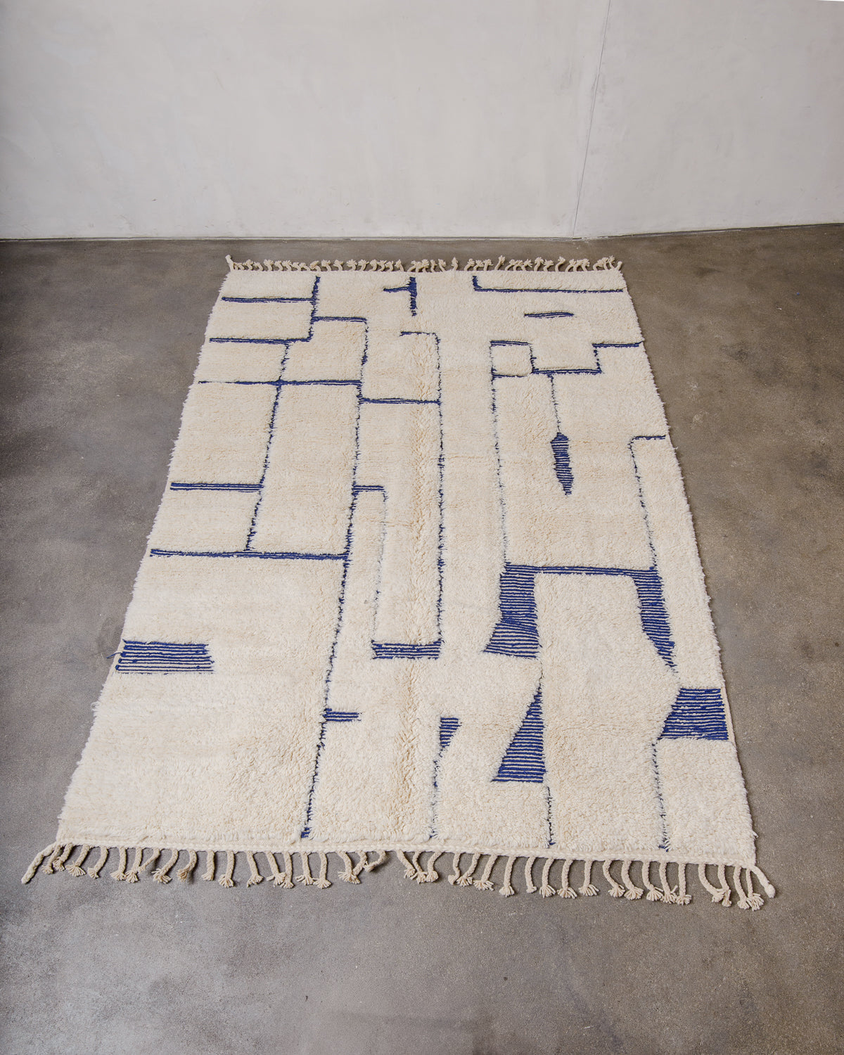 Cream and blue wool rug with a design made of a mix of high pile and flat woven areas laying flat on concrete floor.